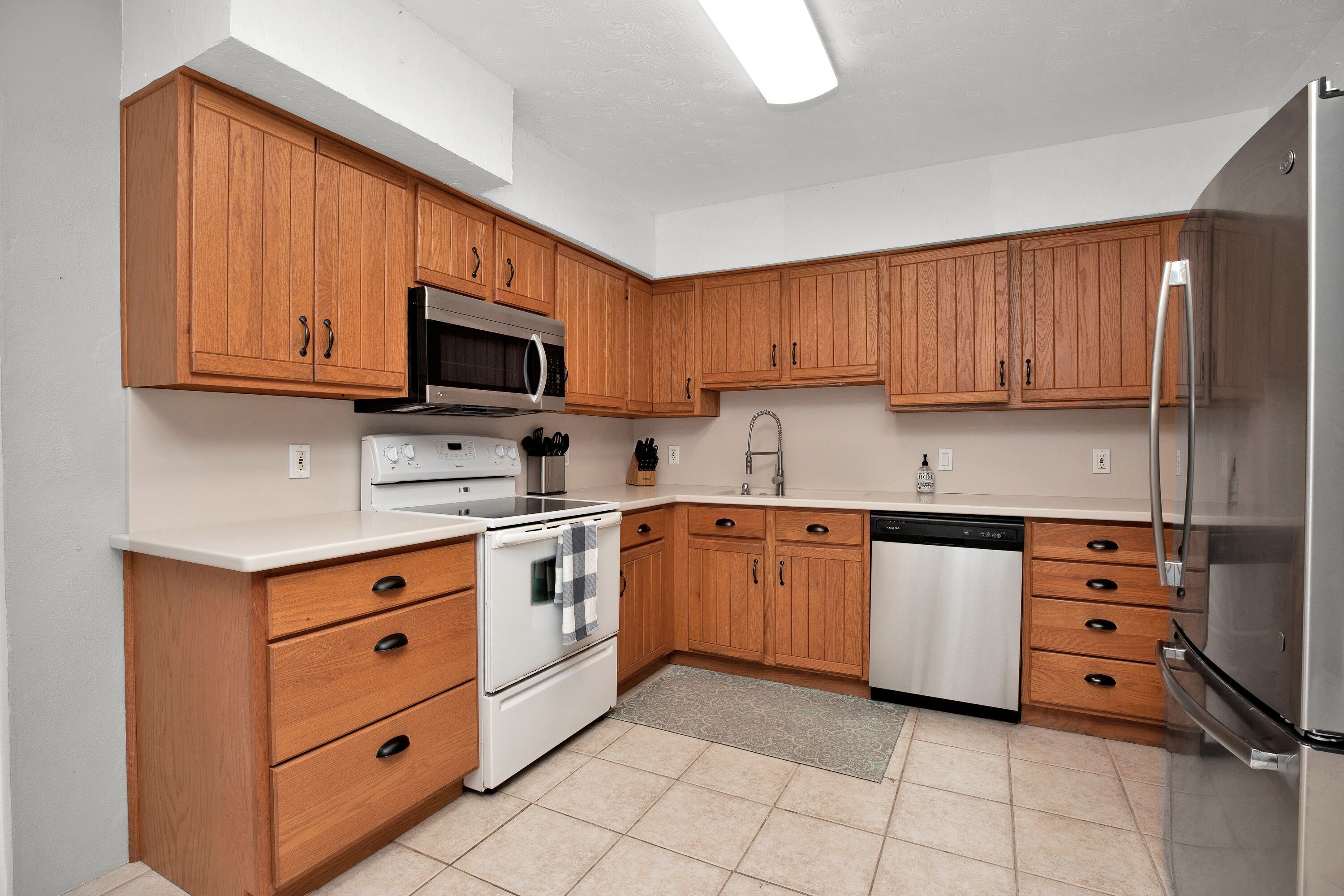A modern kitchen with wooden cabinets, stainless steel appliances, and a tiled floor.