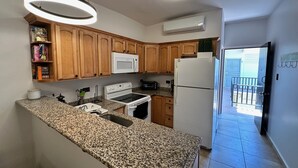 Une cuisine dotée de plans de travail en granit, de meubles en bois, d’une cuisinière blanche, d’un four à micro-ondes, d’un réfrigérateur et d’un climatiseur.