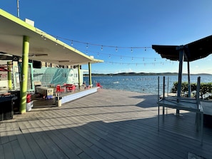 A wooden deck with outdoor seating, a view of the water, and a building with a green facade.