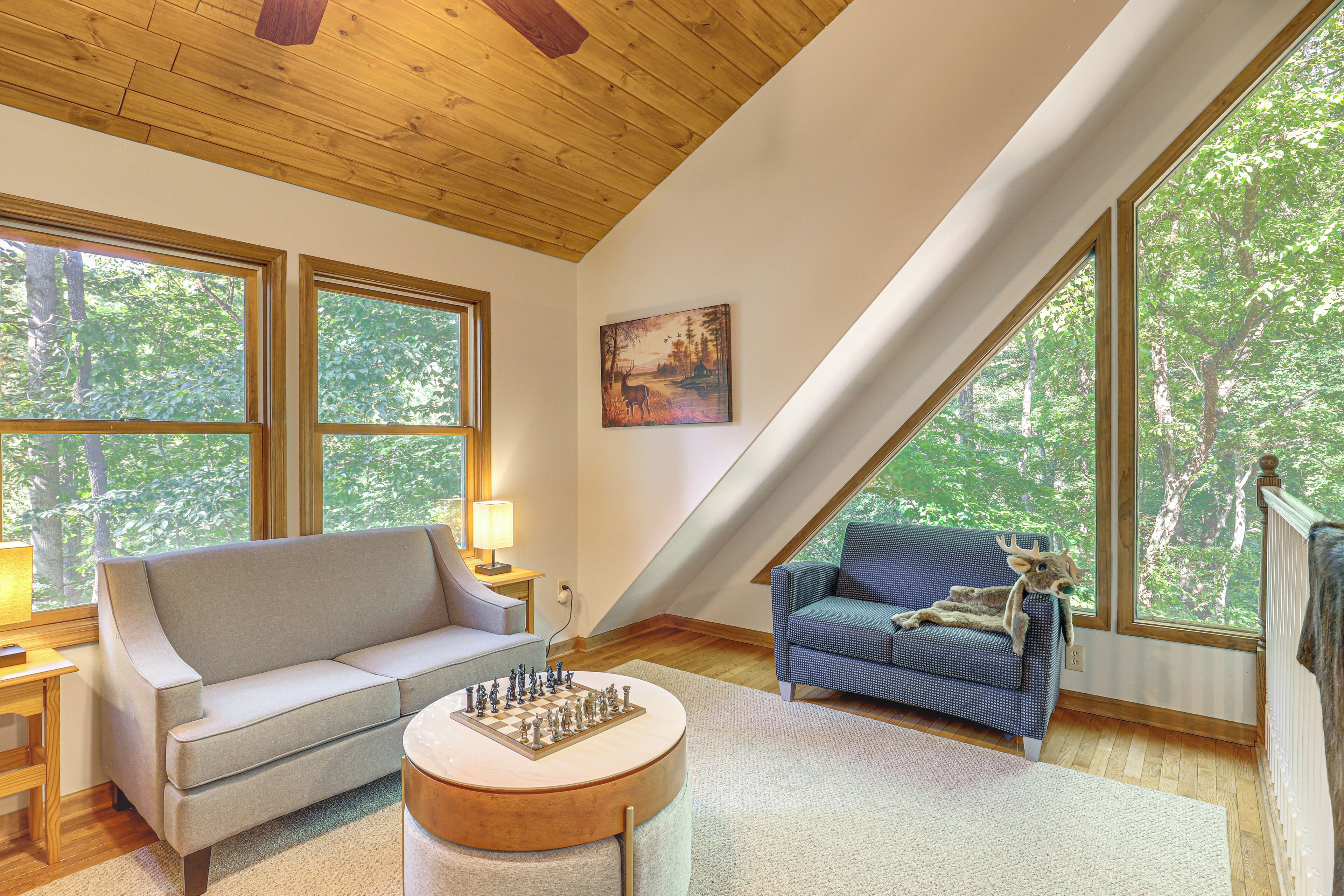 A loft-style room with a wooden ceiling, large windows, a sofa, a chair, a round coffee table, and a chessboard.