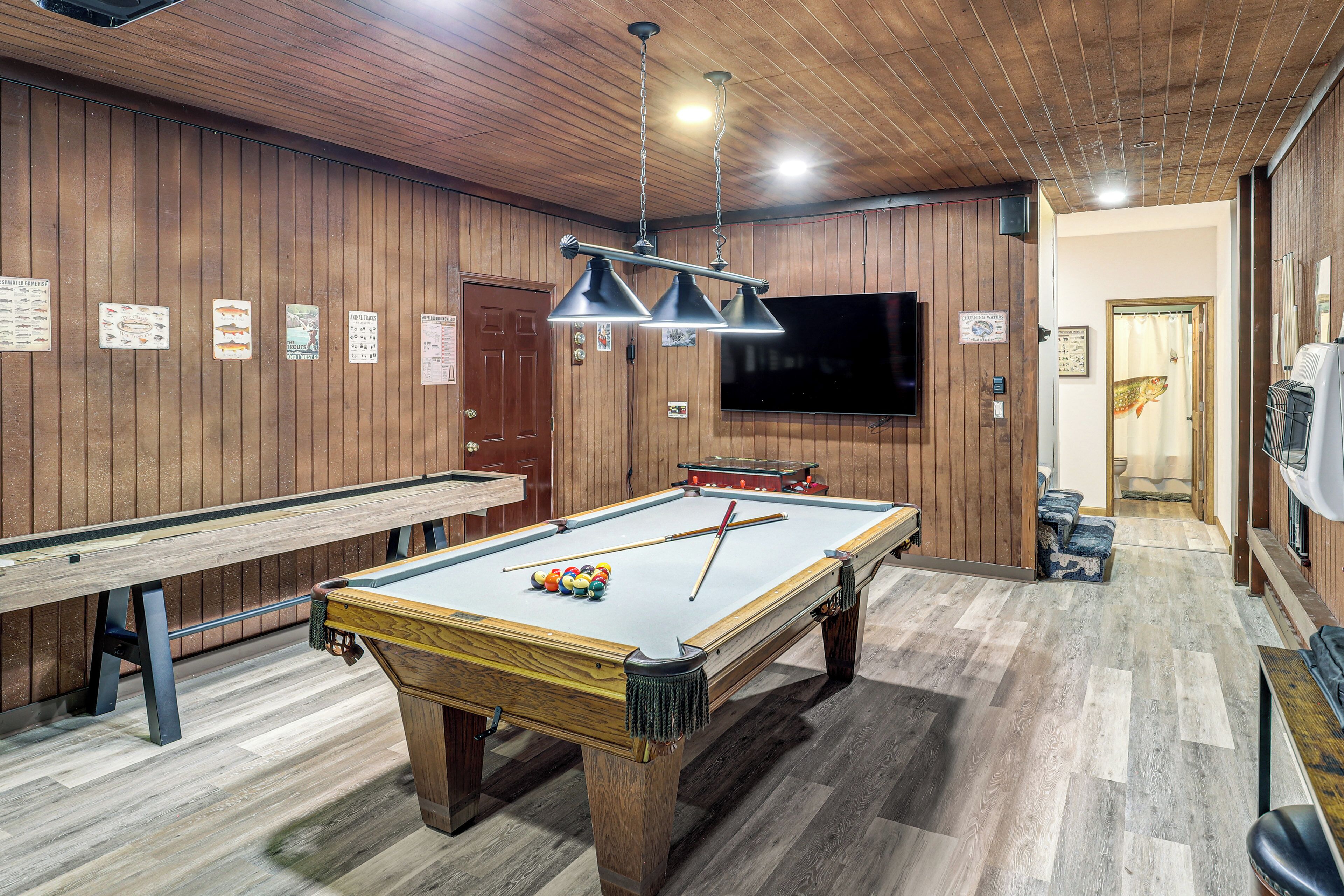 A pool table with billiard balls, a pool cue, and a television mounted on the wall.