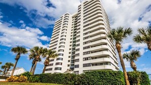 A high-rise hotel with multiple balconies, surrounded by palm trees and a well-maintained hedge. - Life is better at the Beach (Daytona Beach)