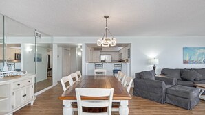 A spacious living room with a wooden dining table, white chairs, and a grey sofa. - Life is better at the Beach (Daytona Beach)