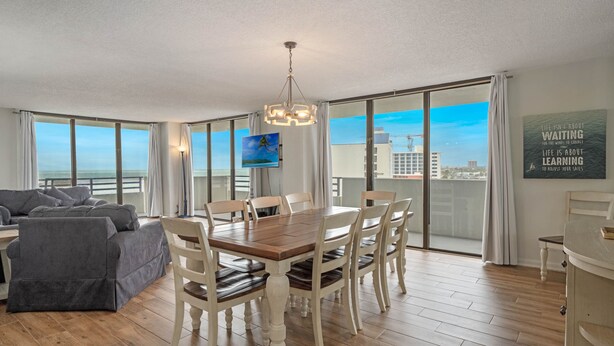 A modern living room with a dining area, large windows, and a view of the city. - Life is better at the Beach (Daytona Beach)