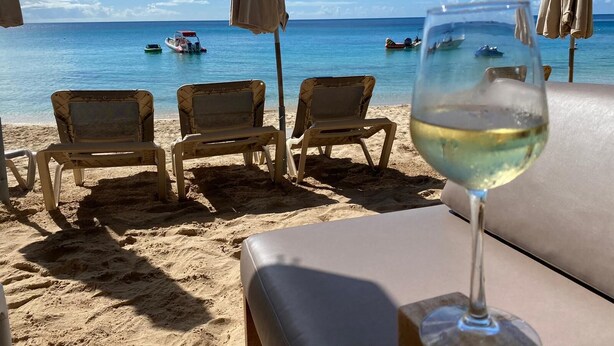 Blick auf den Strand mit Liegestühlen und einem Glas Weißwein.