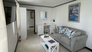 Ein modernes Wohnzimmer mit grauem Sofa, einem weißen Couchtisch, einem Schreibtisch mit Schubladen und einem Bild an der Wand.