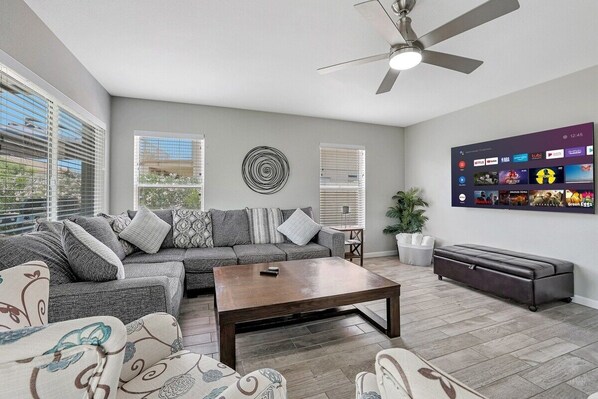 A modern living room with a sectional sofa, a coffee table, and a TV mounted on the wall displaying various streaming services.
