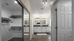 Een gang die leidt naar een badkamer met een spiegel, wastafel en een deur.