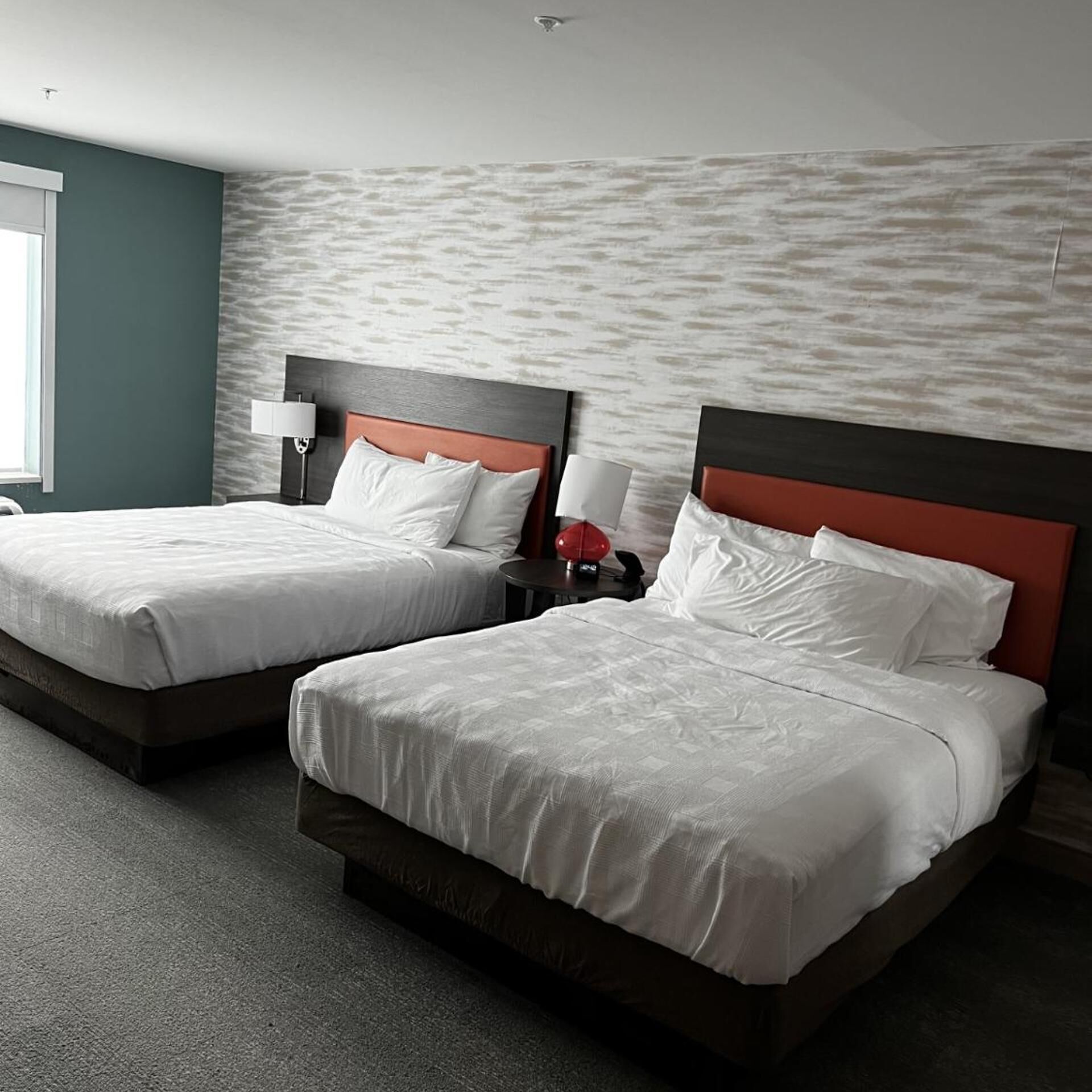 A hotel room with two beds, a nightstand with a lamp, and a textured wall.