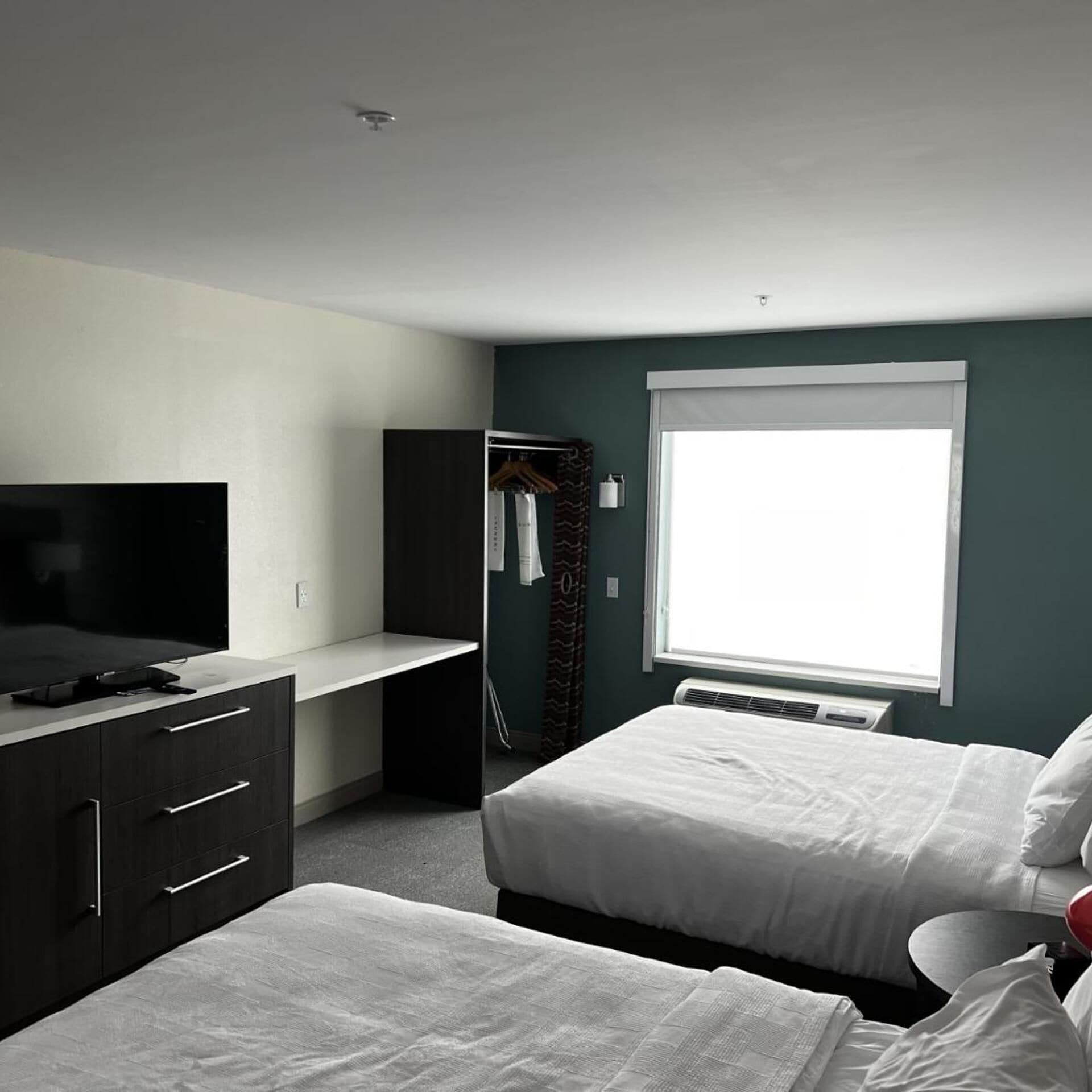 Une chambre d’hôtel avec un lit, un bureau avec une télévision, une fenêtre et une armoire.
