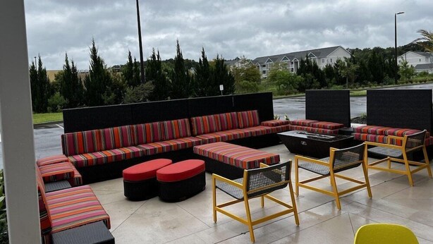 An outdoor seating area with a sofa, ottomans, and chairs, a fire pit, and a view of a residential area. - Home2 Suites BY Hilton Hinesville (HINESVILLE)