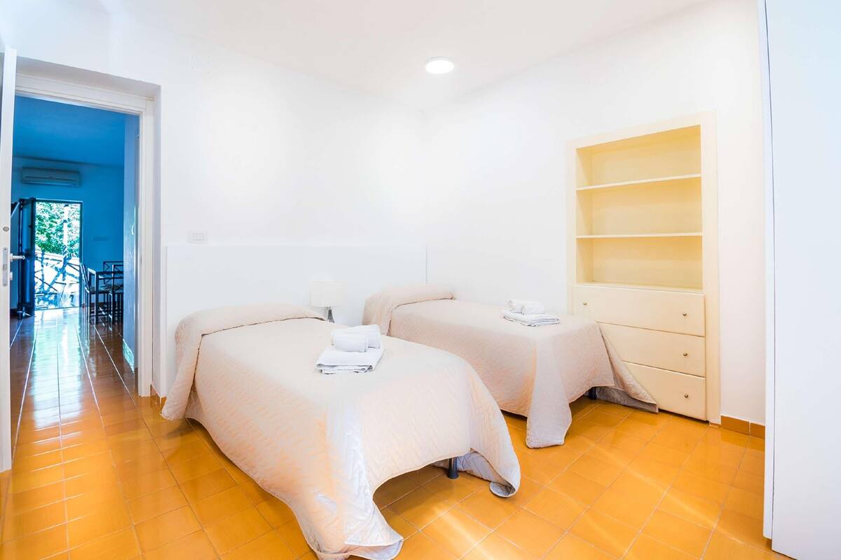 A hotel room with two beds, a wardrobe, and a view of the outside.