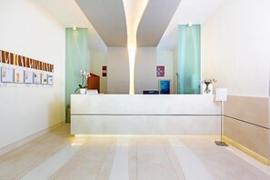 A modern reception desk with a light wood finish, a glass partition, and a framed photo display on the wall. - Residence Le Axidie Sure Hotel Collection by BW (Vico Equense)