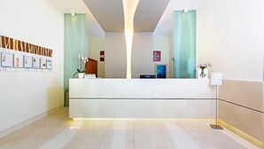 A modern reception desk with a light wood finish, a glass partition, and a framed photo display on the wall. - Residence Le Axidie Sure Hotel Collection by BW (Vico Equense)