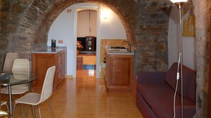 A living room with a stone archway, a dining area with wicker chairs, a sofa, and a kitchen in the background. - Residence Le Axidie Sure Hotel Collection by BW (Vico Equense)