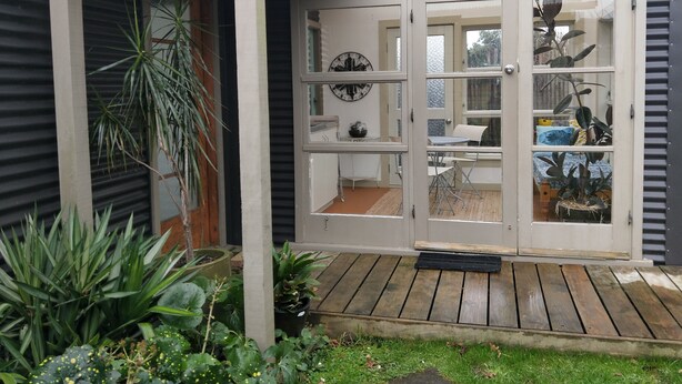 Una casa con terraza de madera, puerta de vidrio con un reloj y plantas en macetas.