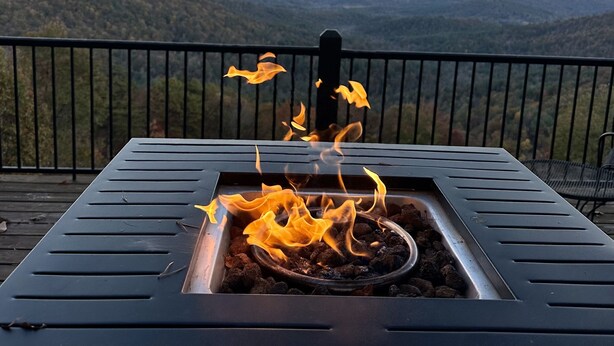 A metal fire pit with flames, surrounded by a metal railing, overlooking a mountainous landscape.