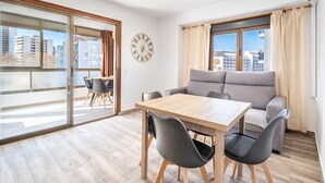 A modern living room with a wooden table and chairs, a grey sofa, and a large window with curtains. - Waldorff 4-A (Benidorm)