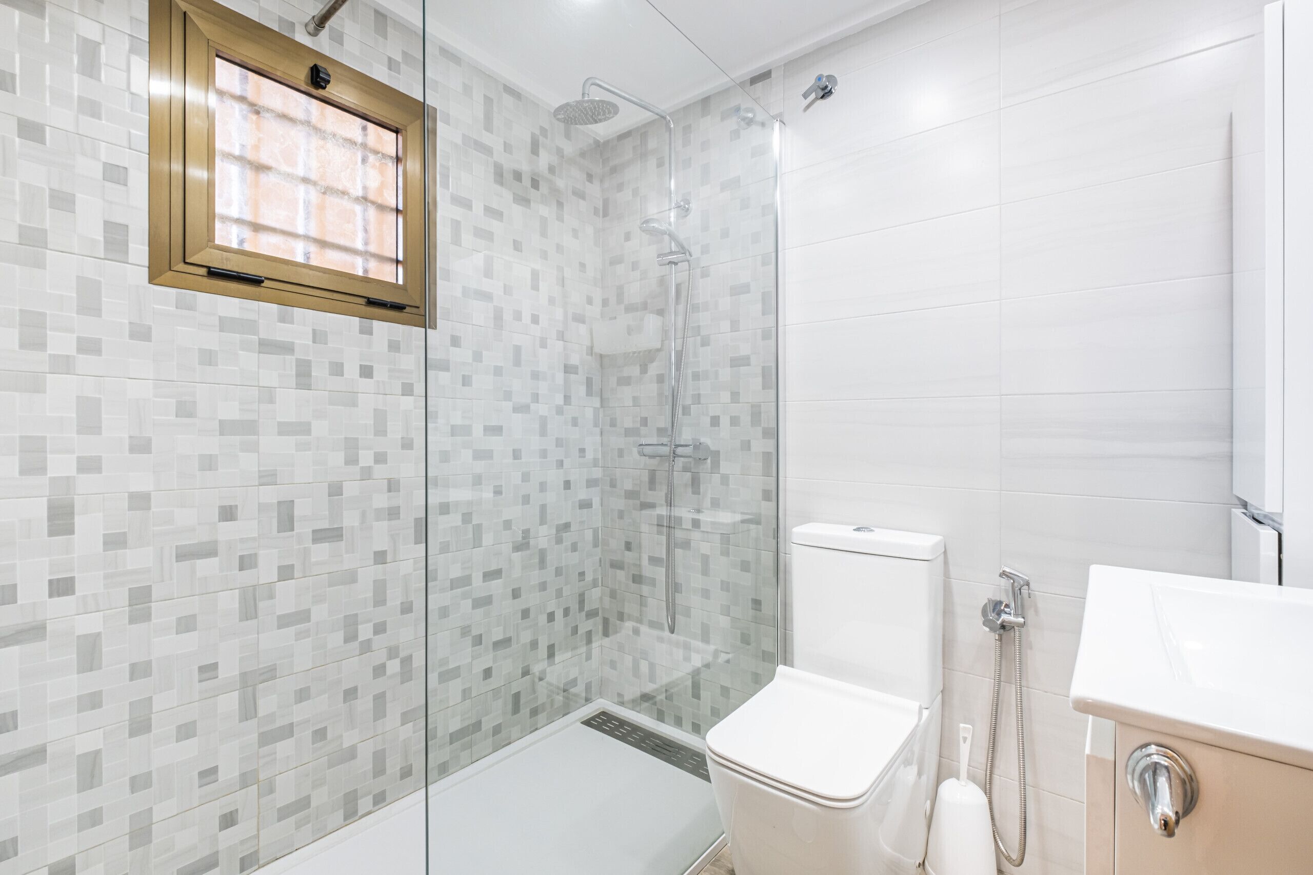 Une salle de bain moderne dotée d’une douche à parois de verre, de toilettes et d’un lavabo.