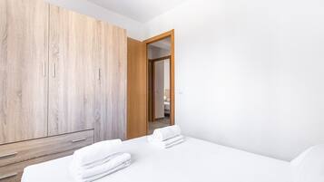 A hotel room with a wooden wardrobe, a bed with white linens, and a view into the adjacent room.