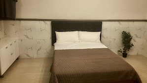 A bedroom with a bed, a nightstand, a potted plant, and a hanging garment.