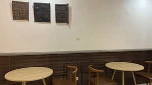 A restaurant interior with three wooden tables and chairs, a dark tiled backsplash, and decorative wall panels.
