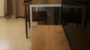 A room with a wooden table, two chairs, a TV, and a curtain.
