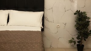 A bed with a patterned bedspread, a headboard, and a potted plant beside a marble wall.