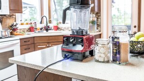 Une cuisine avec un mixeur Vitamix posé sur le comptoir, un bocal de guimauves, un bocal de café et un panier de pommes.