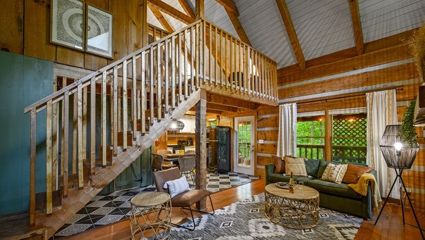 Ein Holzblockhaus-Interieur mit Treppe, Essbereich und Wohnzimmer mit Sofa und Couchtisch.
