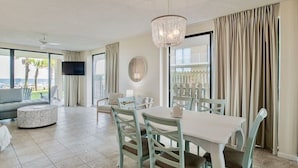 A spacious living room with a dining area, large windows, and a view of the ocean. - Summer House 106B | Ground floor, wrap around deck, direct beach front! (Orange Beach)