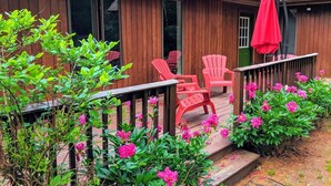 Una casa de madera con un porche, sillas rojas y flores rosadas.