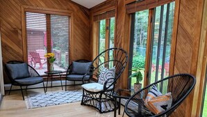 Una habitación con paneles de madera, dos sillas de mimbre negro, una mesita y una planta en maceta.