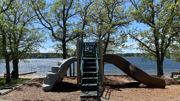 Ein Spielplatz mit Rutsche und Klettergerüst in der Nähe eines Sees.