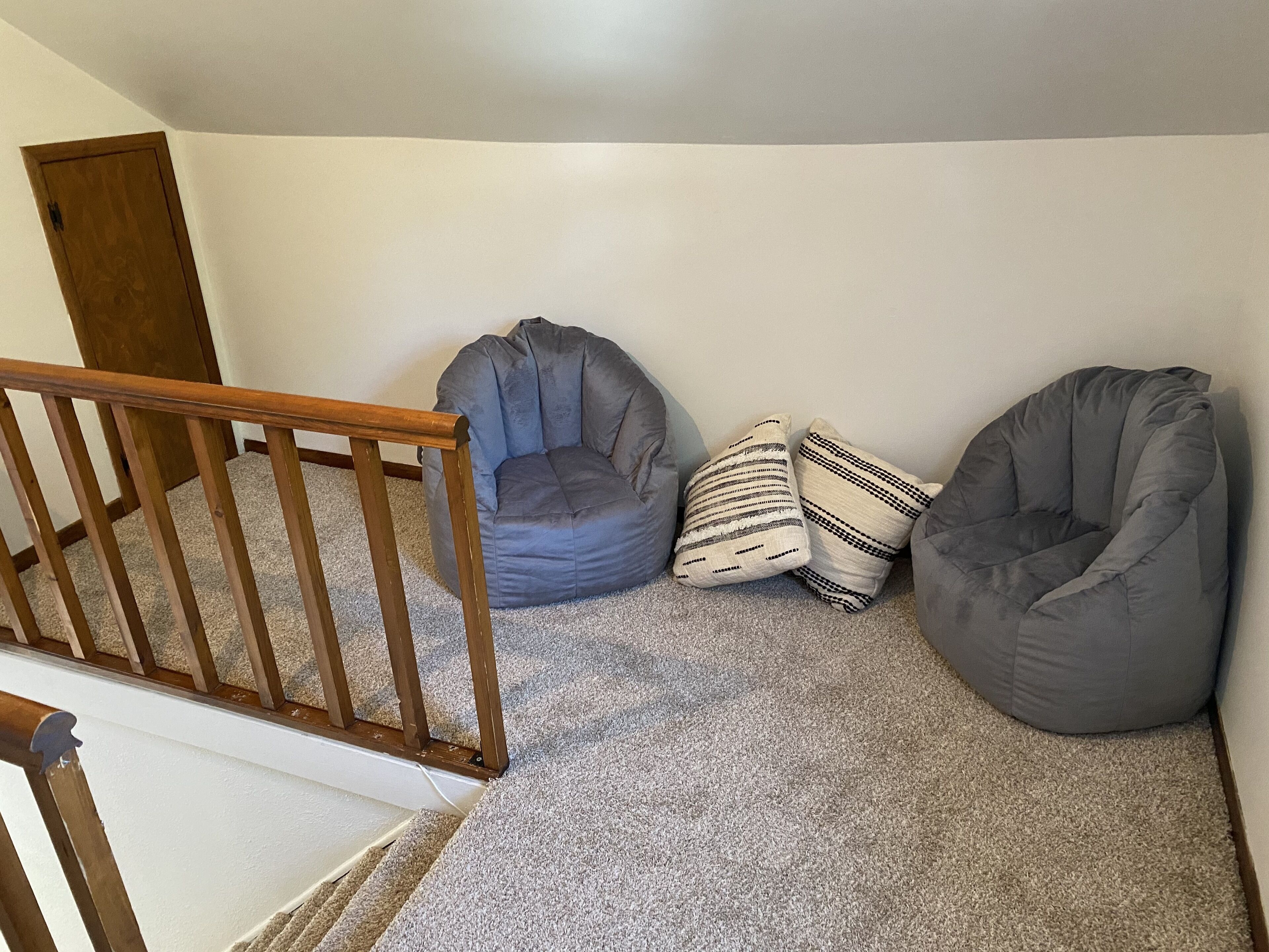 A corner room with a grey carpet, a wooden staircase, and two bean bag chairs.
