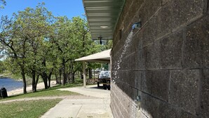 Ein Betonweg führt zu einer überdachten Fläche mit einer Bank, einem Tisch und einer Mauer.