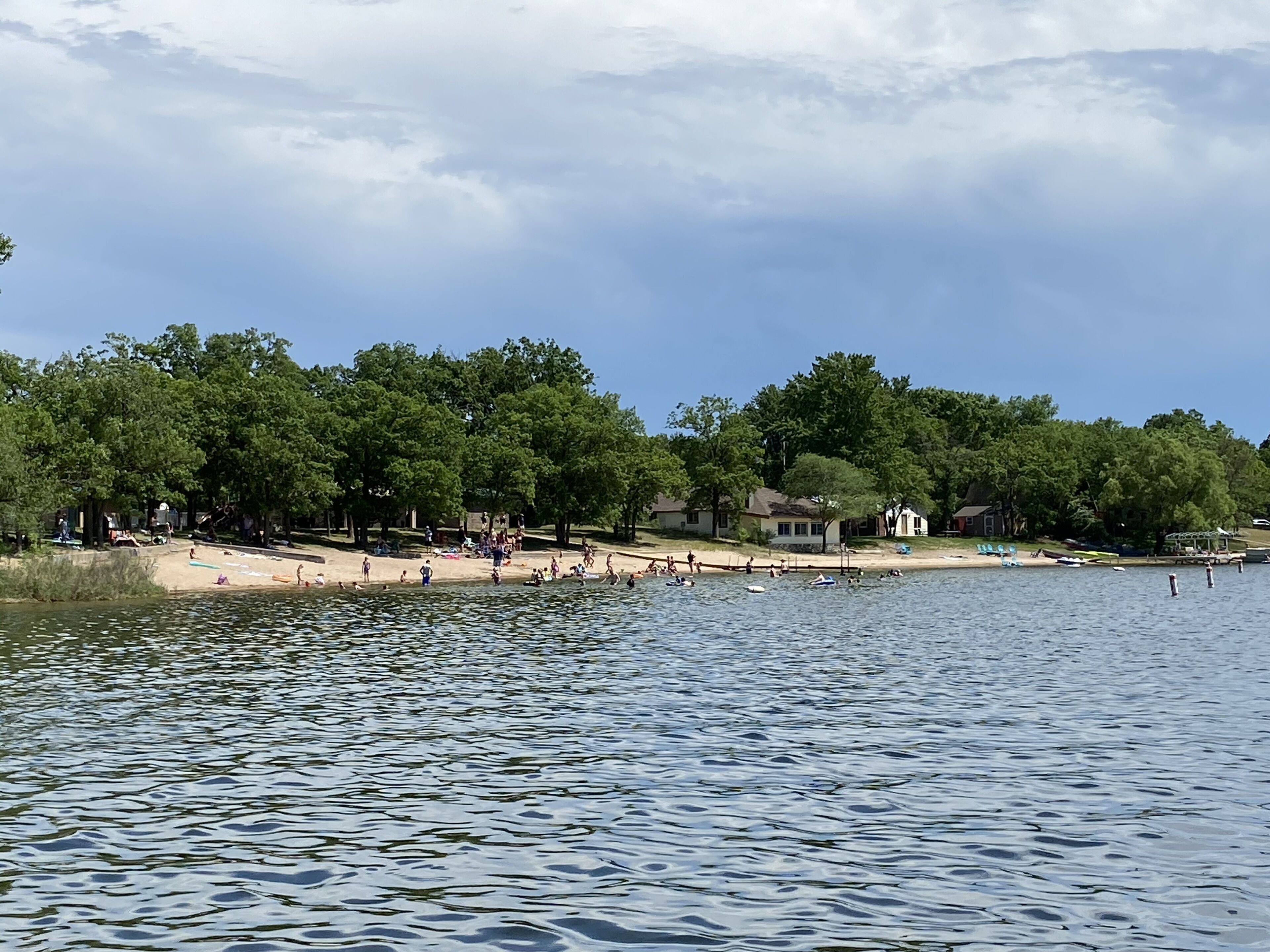 Une vue sur le lac, avec une plage de sable, des arbres et des maisons en arrière-plan.