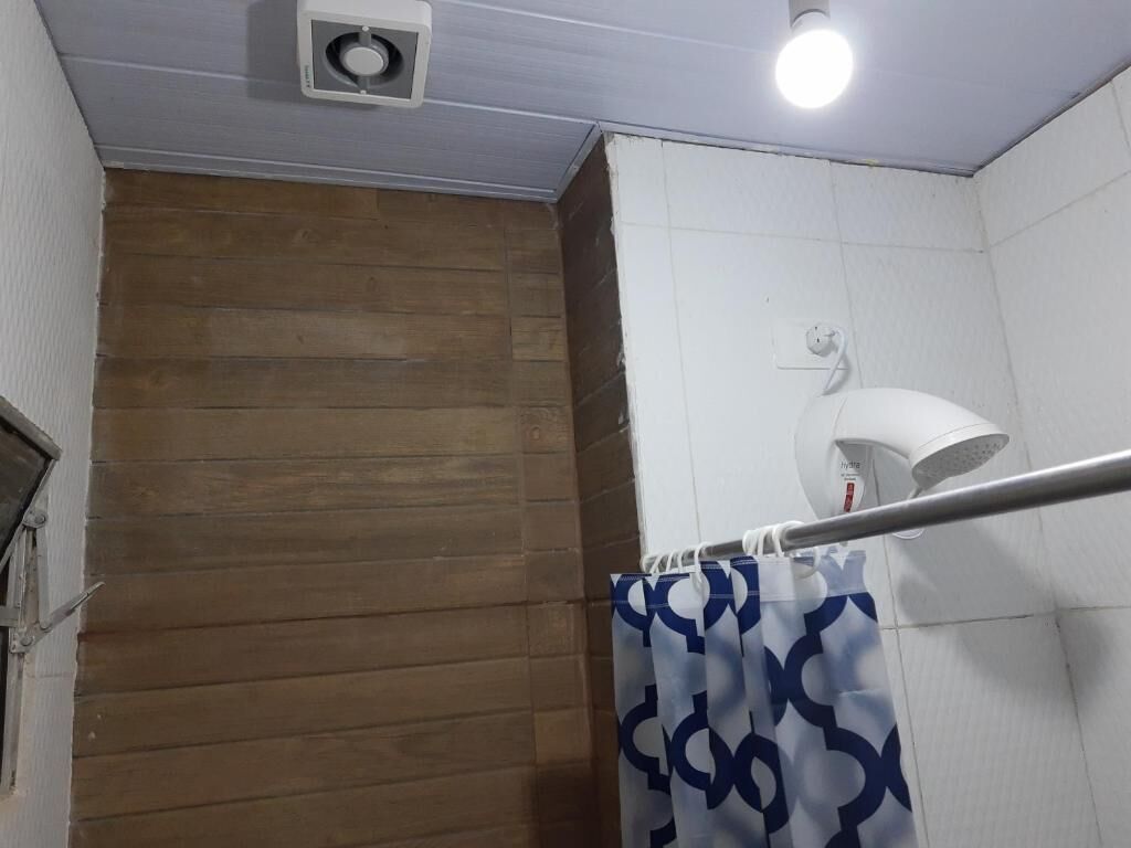 Un baño con pared de madera, pared de azulejos blancos, zona de ducha y una lámpara en el techo.