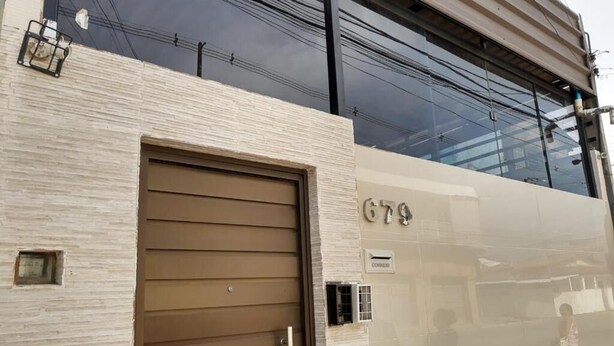 A building with a large garage door, a reflective facade, and a visible number "679". - Lar Recife Olinda - Casa Inteira (Recife)