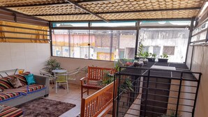 A cozy living area with a sofa, chairs, a wooden bench, and a black metal cage with plants. - Lar Recife Olinda - Casa Inteira (Recife)