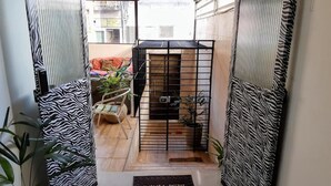 A narrow hallway with zebra-patterned walls, a small seating area with a sofa and cushions, and a door leading to a room with a bed and a window. - Lar Recife Olinda - Casa Inteira (Recife)