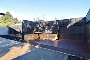 A wooden deck with built-in seating, a brick pathway, and a metal fence.