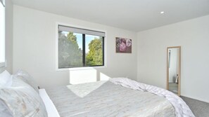 A bedroom with a bed, a window, a painting, and a mirror.