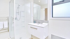 A modern bathroom with a glass shower enclosure, a white vanity with a mirror, and a towel rack.