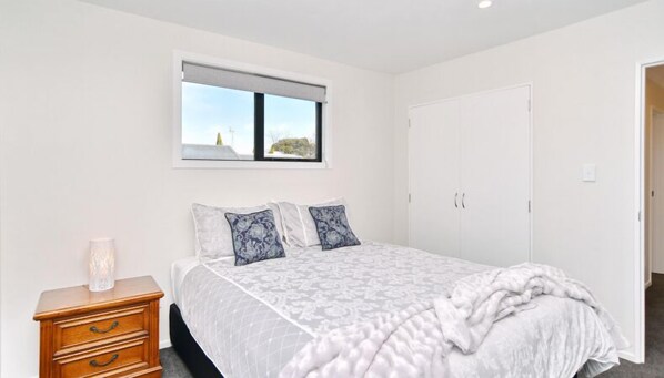 A bedroom with a bed, a nightstand, a window with a view, and a wardrobe.