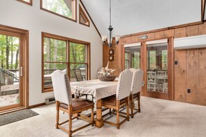 A dining area with a wooden table and chairs, large windows, and a chandelier. - Lakefront Poconos,   Early check in late check out during winter months. (Gouldsboro)