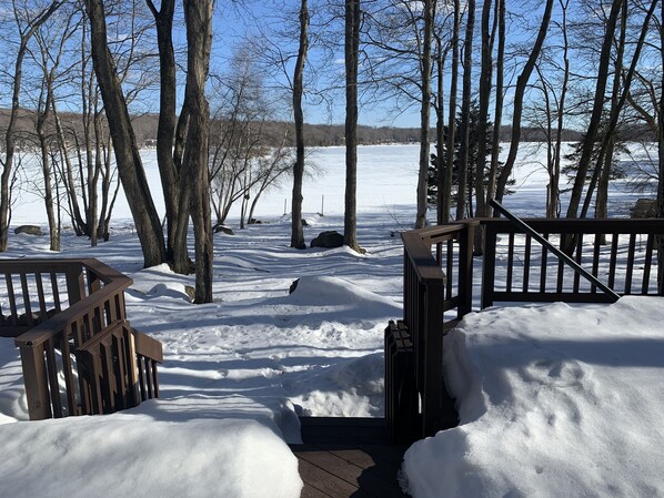 A wooden deck leading to a snowy landscape with trees and a body of water in the background. - Lakefront Poconos,   Early check in late check out during winter months. (Gouldsboro)