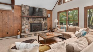 Una sala de estar acogedora con una chimenea de piedra, un televisor grande y un sofá beis de aspecto cómodo.