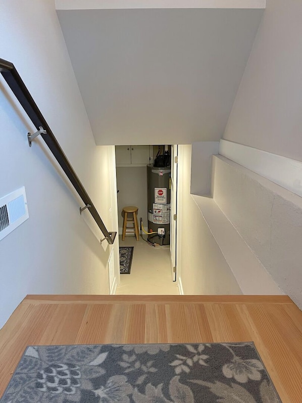 A staircase leading to a small kitchen area with a stool and a water heater.
