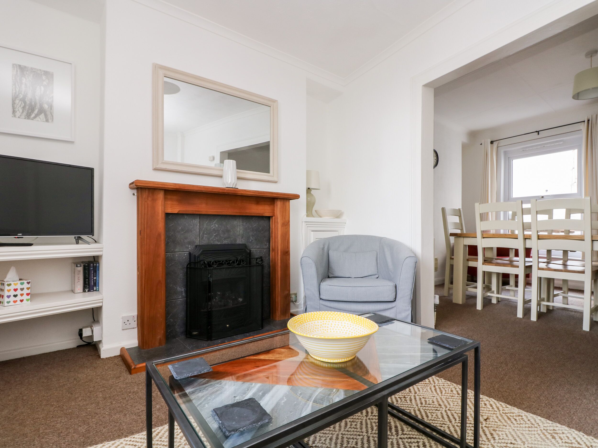 Una sala de estar con chimenea, televisor, una mesa de centro de vidrio y un comedor con sillas.